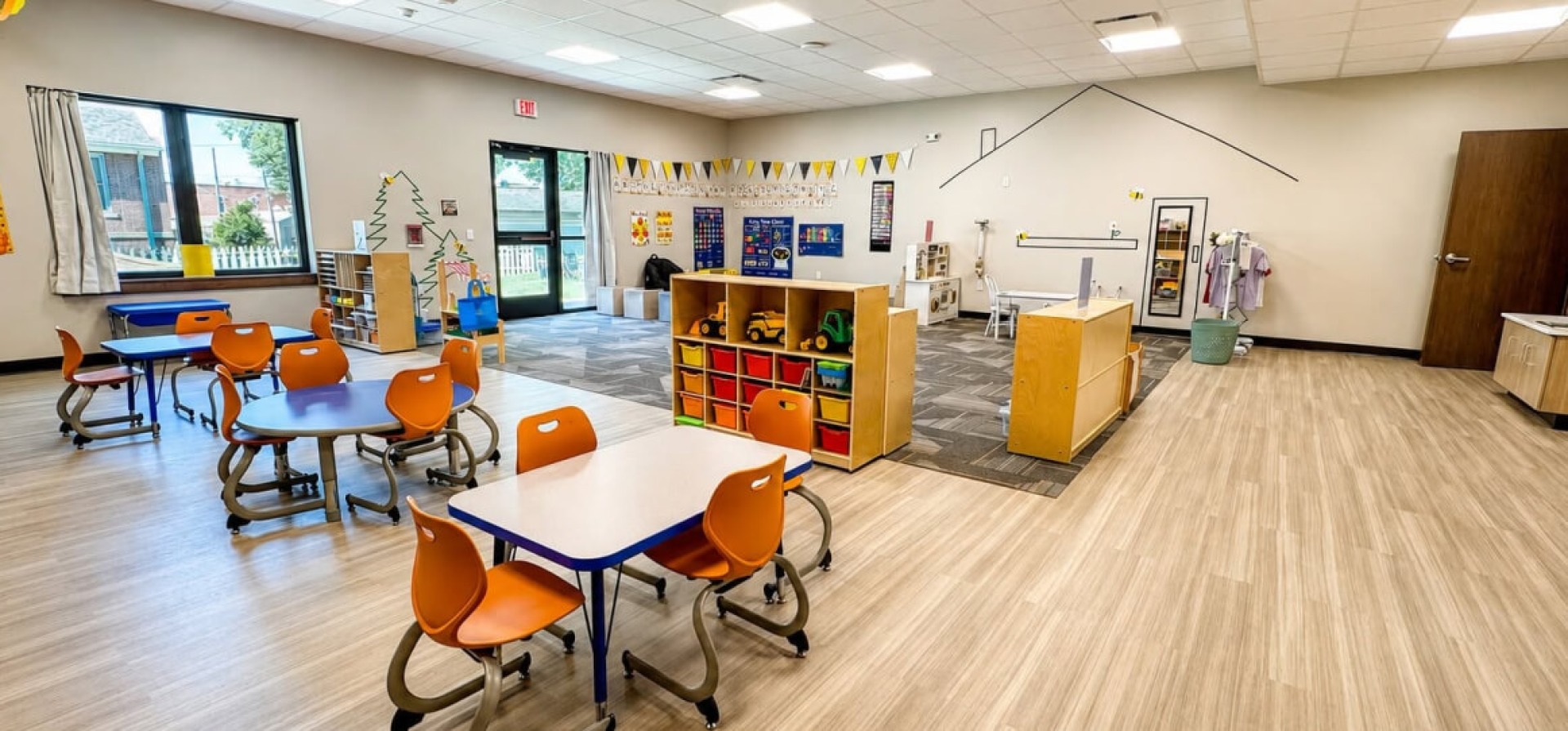 A bright room in Colfax-Mingo Childcare with small tables and chairs, cubbies, play areas, and educational charts on the walls.